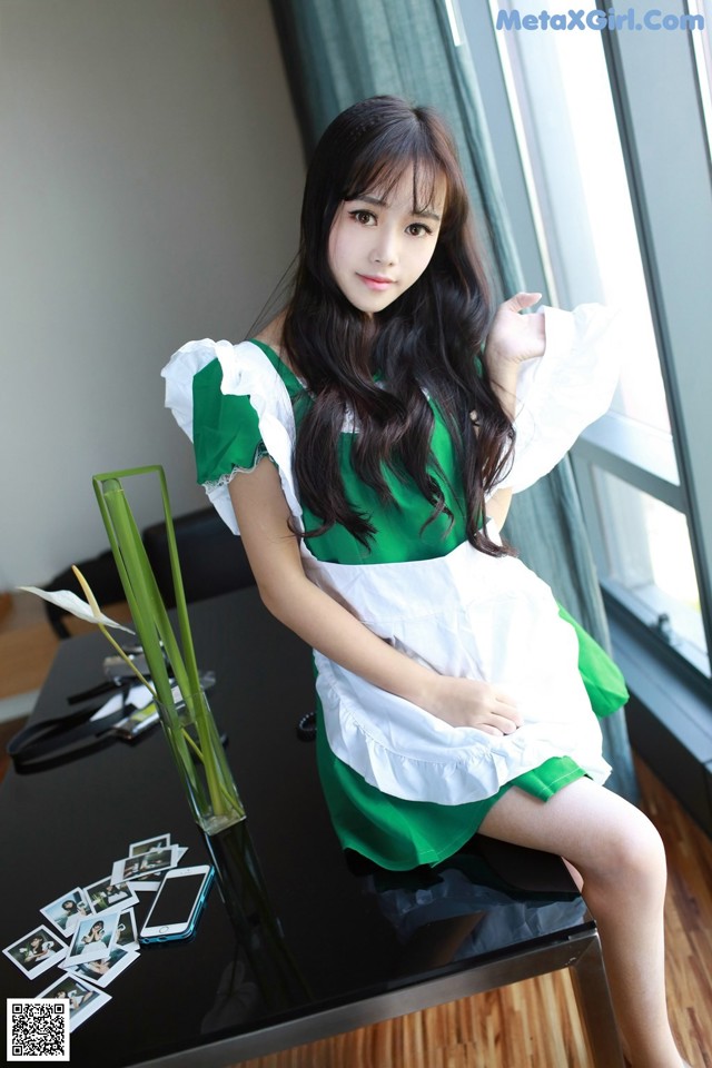 A woman in a green and white dress sitting on a table.