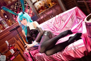 A woman with blue hair sitting on a pink couch.