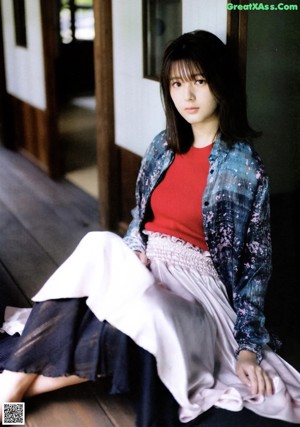 A woman in a pink and blue dress leaning against a wall.