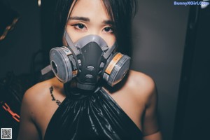 A woman wearing a gas mask sitting on a bed.