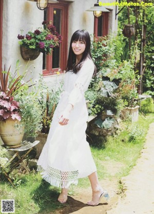 A woman in a white blouse standing in front of flowers.