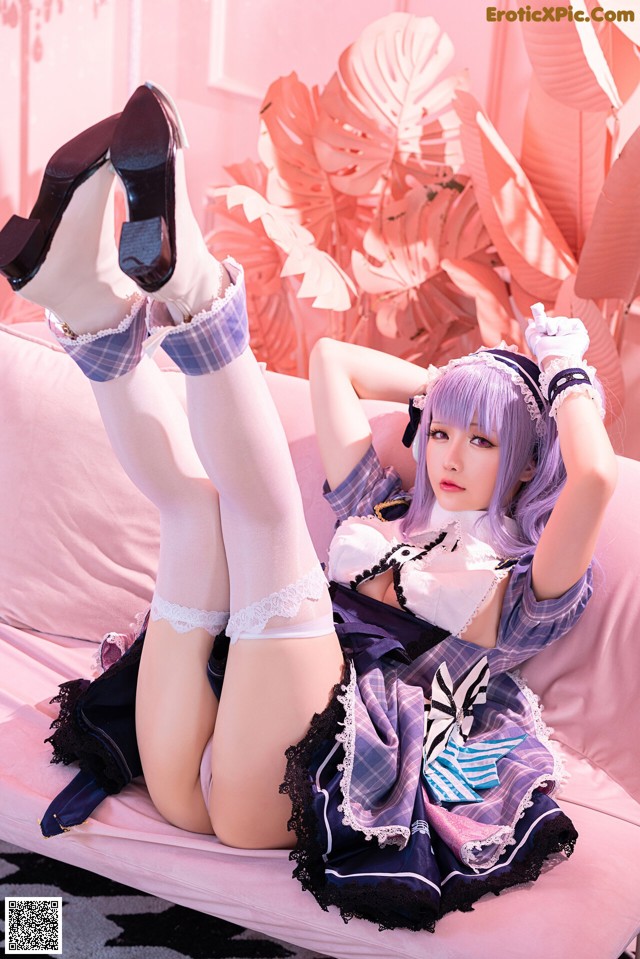 A woman in a maid outfit laying on a pink couch.