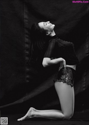 A woman in a black bodysuit sitting on a black background.