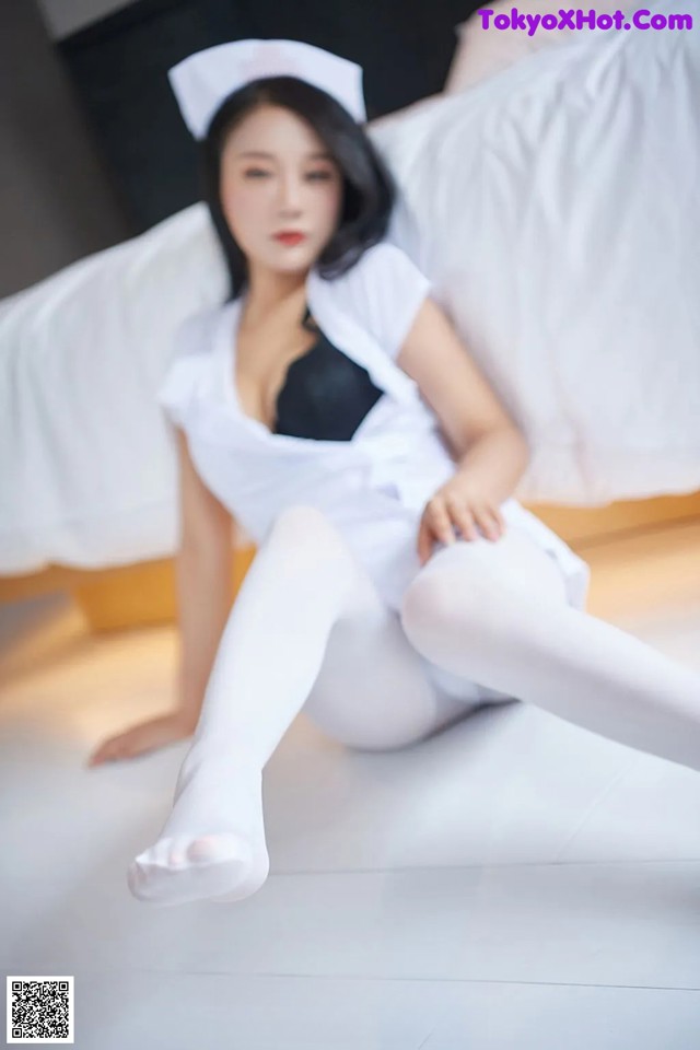 A woman in a white nurse outfit sitting on a bed.
