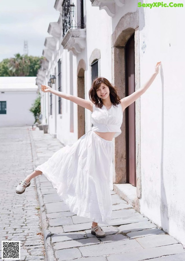 A woman in a white dress is standing on a cobblestone street.