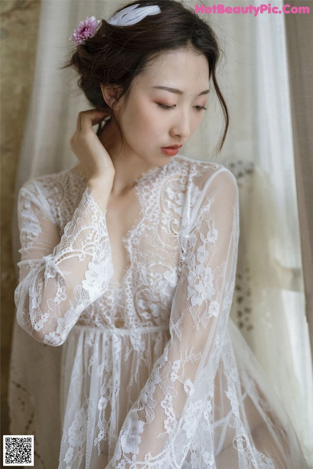 A woman wearing a white lace robe with a flower in her hair.