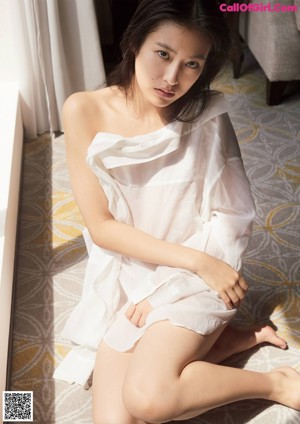 A woman in a white dress standing by a window.