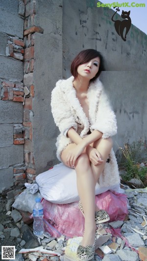 A woman in a white fur coat sitting on the ground.