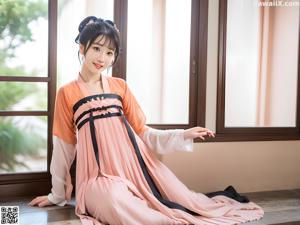 A woman in a blue and pink hanbok posing by the water.