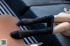 A woman in a black bra and black pantyhose sitting on a couch.