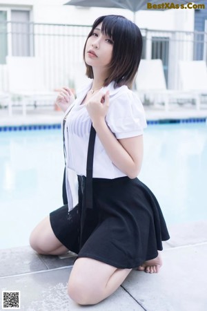 A woman in a white shirt and black skirt by a pool.