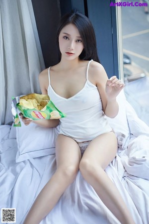 A woman laying on a bed holding a bag of chips.