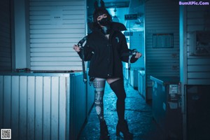 A woman in a black jacket and black boots crouching down on a ledge.