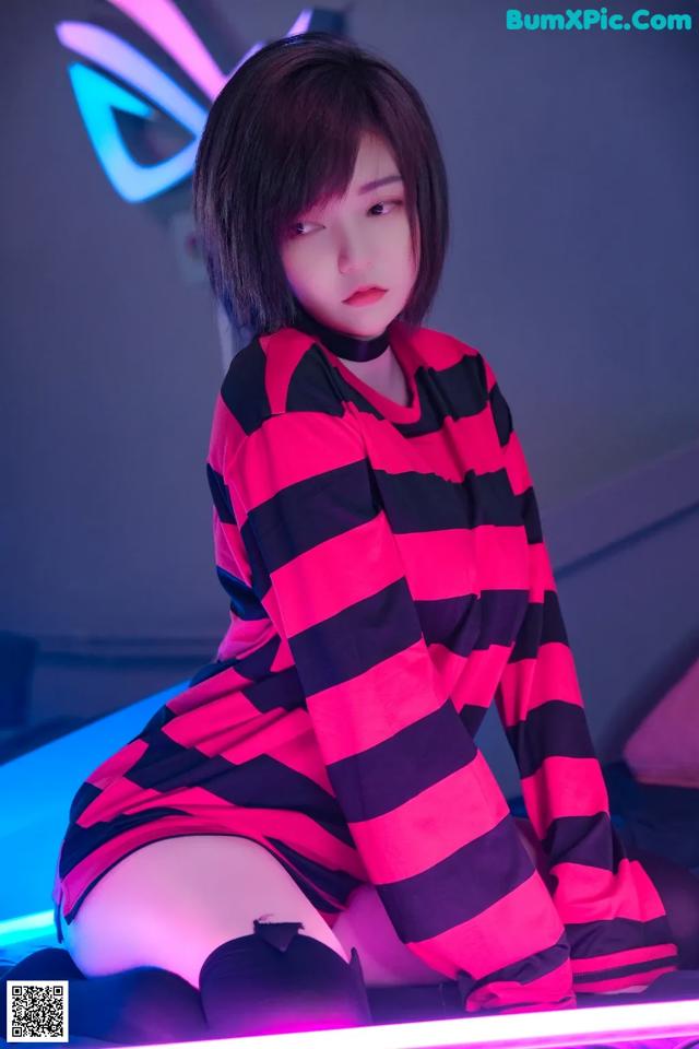 A woman in a red and black striped dress sitting on a bed.