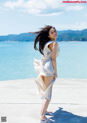 A woman in a white dress is running by the water.