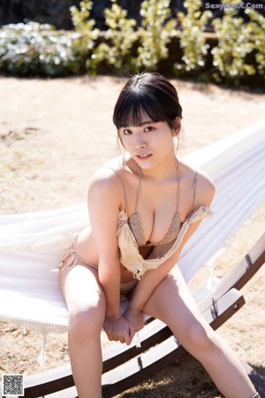 A woman in a bikini sitting on a pile of hay.