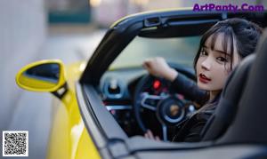 A woman sitting on the ground next to a car.