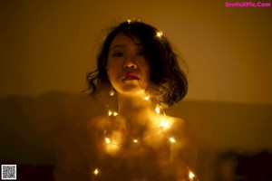 A naked woman sitting on top of a wooden stool covered in lights.