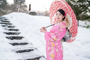 A woman in a pink kimono holding an umbrella in the snow.