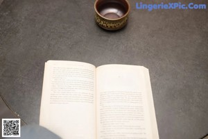 A woman sitting on a desk holding a book.